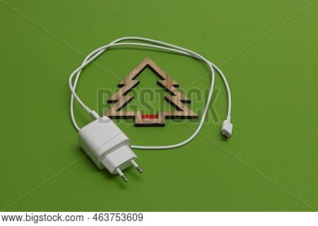 On A Green Background, A Cell Phone Charger And A Christmas Tree In The Form Of An Uncharged Battery