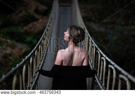 30 Yo White Woman Standing On A Simple Suspension Bridge Outdoors At Dusk, Kordel, Germany