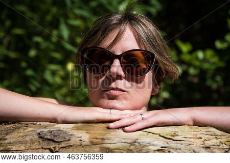 Outdoor Portrait Of A 30 Yo White Woman With Sunglasses, Resting On A Tree Trunk, Kordel, Germany