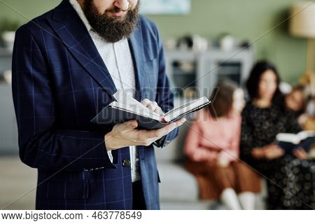 Cropped Shot Of Bearded Jewish Man Reading Book At Home With Family In Background, Copy Space