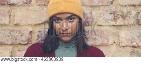 Sad And Serious Latin American Young Adult Woman With Bobble Hat Outdoor In City In Winter