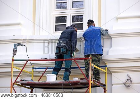 Two Workers Repair The Building Wall Standing On Lifting Platform. Builders Painting The House Facad