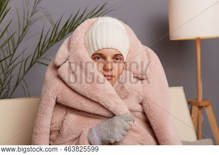 Closeup Portrait Of Cold Frozen Woman Wearing Warm Clothes And Wrapped In Coat Sitting In Room Near 