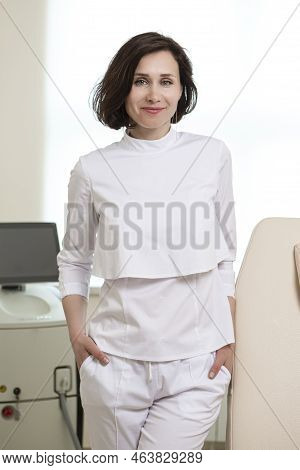 Business Portraits. Confident Female Doctor Posing In Doctor's Smock With Hands Folded In Front Agai