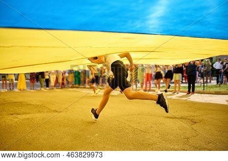Zdolbuniv, Ukraine, 23.08.2022: A Girl Runs Under The Flag Of Ukraine On Flag Day. Its A Festive Day