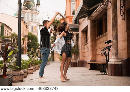 Young Couple With Umbrella Dancing Under Rain On City Street