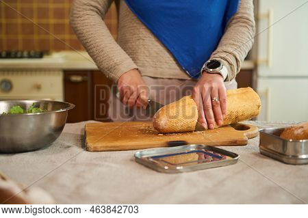 Cropped View Of A Woman, Housewife In A Blue Hijab Cutting Loaf Of Whole Grain Sourdough Wheat Bread