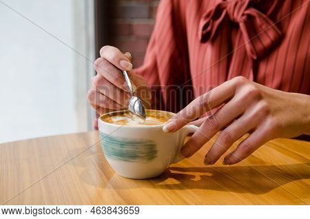 Young Female Hands With Long Fingers Holding Cup Of Coffee With Latteart At Wooden Table In Cafe, Wo