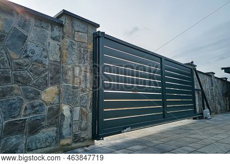 Wide Automatic Sliding Gate With Remote Control Installed In High Stone Fense Wall. Security And Pro
