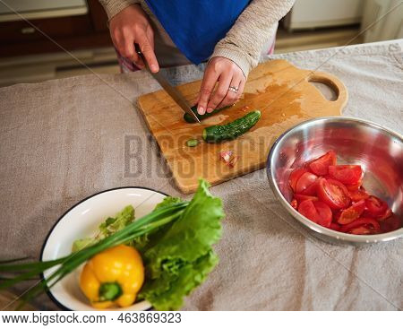 Close-up. Top View Of A Woman Housewife Using A Kitchen Knife, Cutting Fresh Cucumbers On A Wooden C