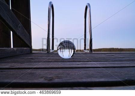 Glass Ball On A Wooden Pier At A Swedish Lake At Evening Hour. Nature Shot From Scandinavia