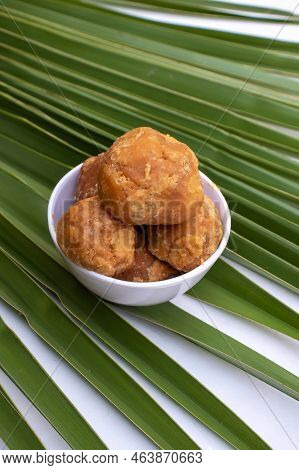 Indian Palm Jaggery Or Gur In A White Bowl Isolated On A Palm Leaf In Vertical Orientation