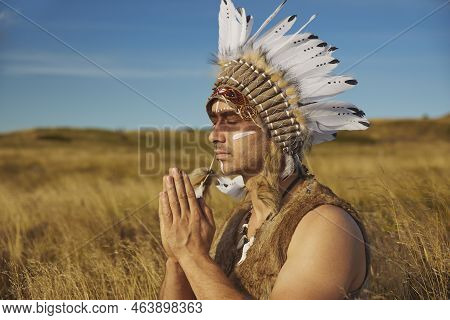 A Man In Traditional Native American Clothing Praying In The Steppe