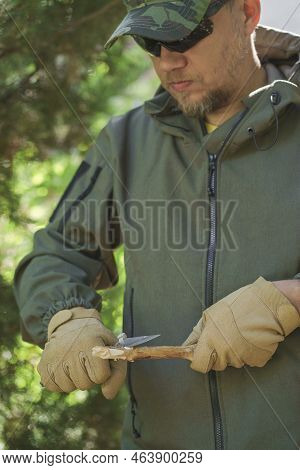 Tourist Man In Green Uniform Planes A Branch With Small Knife. Man In Glasses Dressed In Uniform And