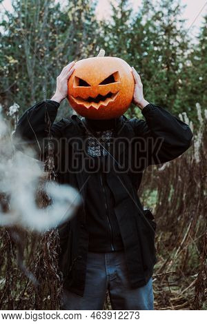 Man With An Orange Pumpkin (jack O Lantern) On His Head In A Black Jacket Stands In The Autumn Dry G