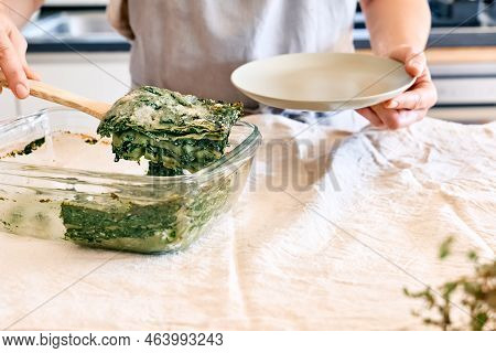 Woman's Hands Putting One Porzione Of Homemade Lasagna With Spinach And Ricotta In A Plate From Glas