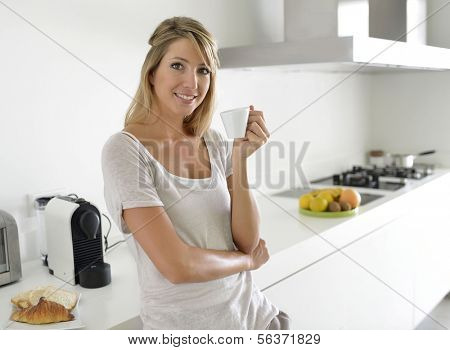 Cheerful young woman having coffee in kitchen