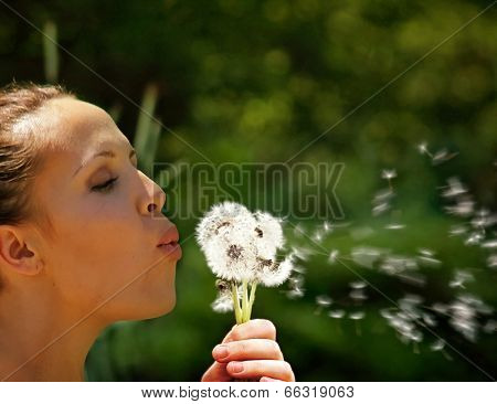 a pretty woman blowing on dandelion weed flowers
