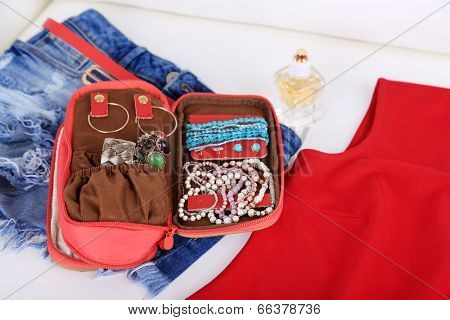 Handbag with accessorises, female clothes and perfumes in bottles on sofa on  home interior background