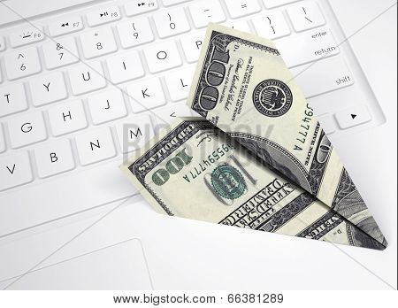 Paper plane from dollar bills lying on keyboard