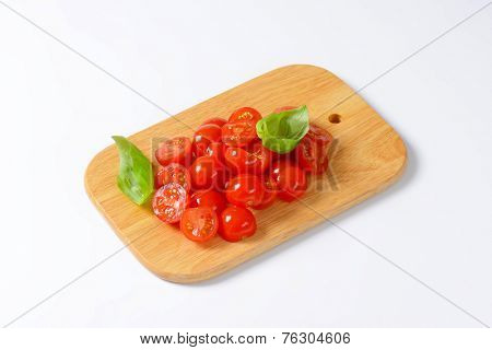 wooden cutting board with halved cherry tomatoes decorated with fresh basil