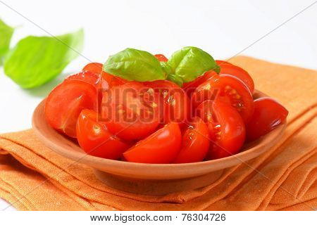 side view of halved cherry tomatoes in the bowl, with basil leaves on the background