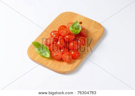 halved cherry tomatoes with basil served on the wooden cutting board