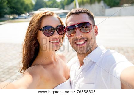 love, wedding, summer, dating and people concept - smiling couple wearing sunglasses making selfie in city