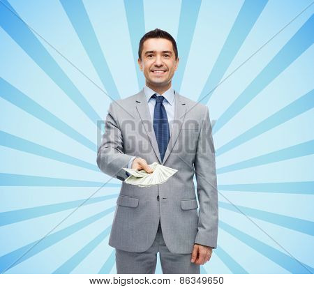 business, people and finances concept - smiling businessman with american dollar money over blue burst rays background