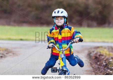 Funny cute preschool kid boy in safety helmet and colorful raincoat riding his first bike