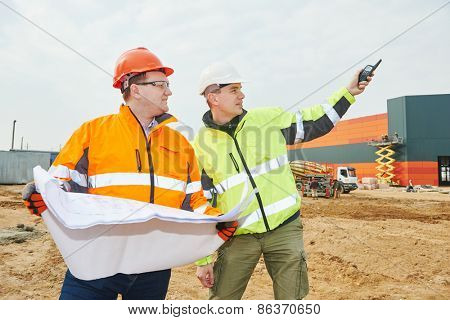 male engineers construction foreman managers outdoors at building site with blueprints