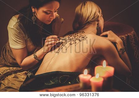 Drawing process of henna menhdi ornament on woman's back 