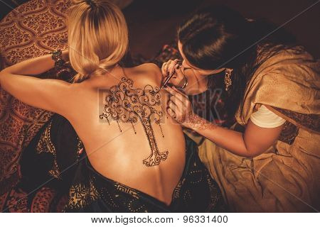 Drawing process of henna menhdi ornament on woman's back 