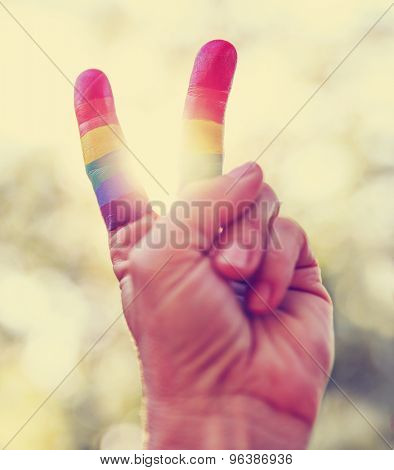  a hand making the V peace sign with fingers painted as the gay rainbow flag with the sun showing through toned with a retro vintage instagram app or action effect 
