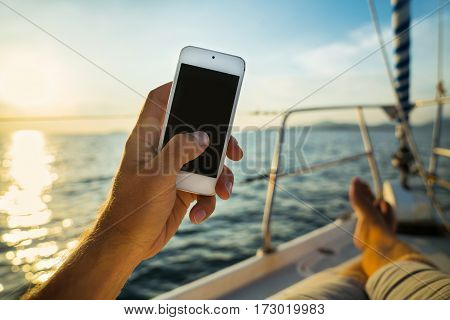 Summer leisure. Rest on a yacht with a phone in his hand. Man lying on the deck and enjoy your smartphone. The guy doing the photo feet on the background seascape and yachts.
