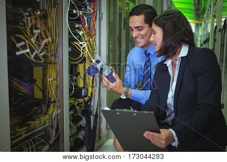 Technicians using digital cable analyzer while analyzing server in server room