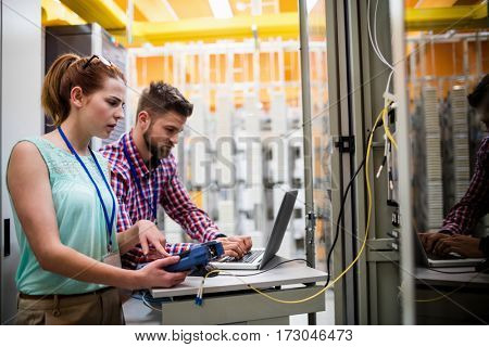 Technicians using laptop while analyzing server in server room