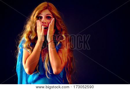 Frightened woman screaming with fear indoor at halloween night. Horror. Girl with tousled hair bawl covered her face on black background.