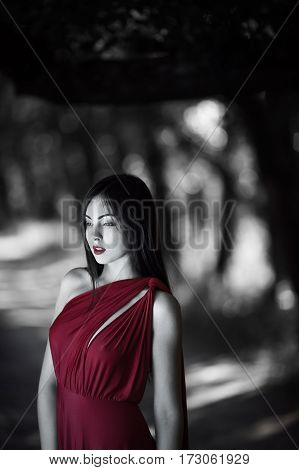 Wonderful sexy fashion model walking in a fantastical forest by footpath.Mystical portrait of sensual seductive woman in luxury long red dress posing against bokeh trees background. Multi-racial Asian Caucasian girl. Fashionable toning. Creative computer 