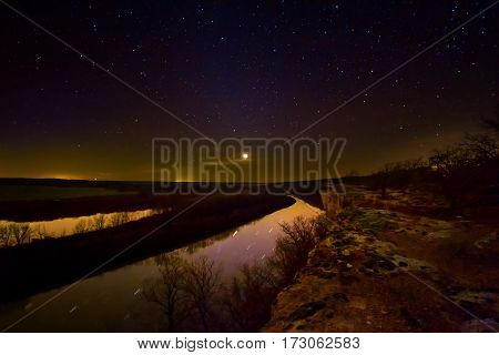 Nightscape of a bluff in the Lake of the Ozarks in Missouri overlooking the Osage River. The planet Uranus is glowing as a few clouds goes in front of it.