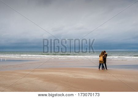 A young couple looking out to the North Sea: Bamburgh Beach, Northumberland, England, UK. March 15 2016.