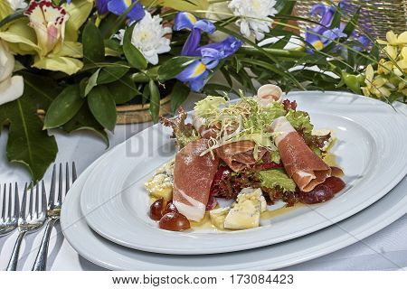 meat salad with ham cheese lettuce Dorblu grapes and olive oil served on a plate on a table with flowers