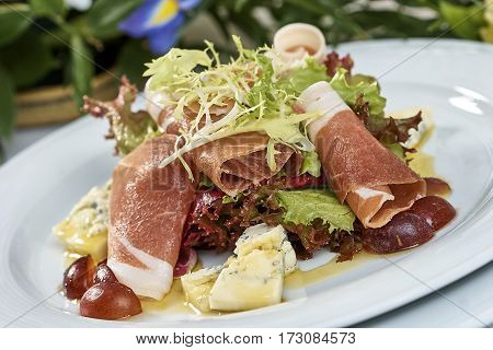 meat salad with ham cheese lettuce Dorblu grapes and olive oil served on a plate on a table with flowers