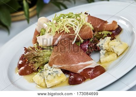 meat salad with ham cheese lettuce Dorblu grapes and olive oil served on a plate on a table with flowers