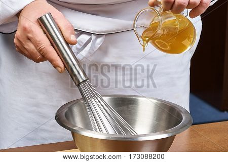 cook hands honey poured from a jug into a bowl of iron for cooking dishes