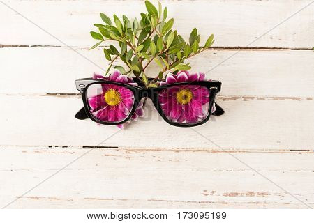 Close-up view of beautiful tender pink flowers in eyeglasses on wooden table spring concept