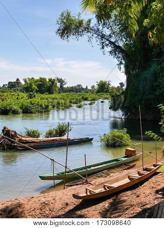 Boat on the side of a river surrounded by plants trees and vegetation in blue sky clouds scenic environment