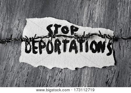 closeup of a barbed wire and a piece of paper with the text stop deportations handwritten in it on a rustic wooden surface