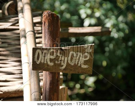 wooden sign directional signpost saying one by one in front of a wooden bamboo bridge