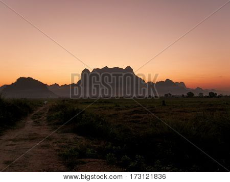 Silhouette of mount zwegabin in Hpa-an Myanmar during morning sunrise with a small path on the left leading into fields close to the mountain